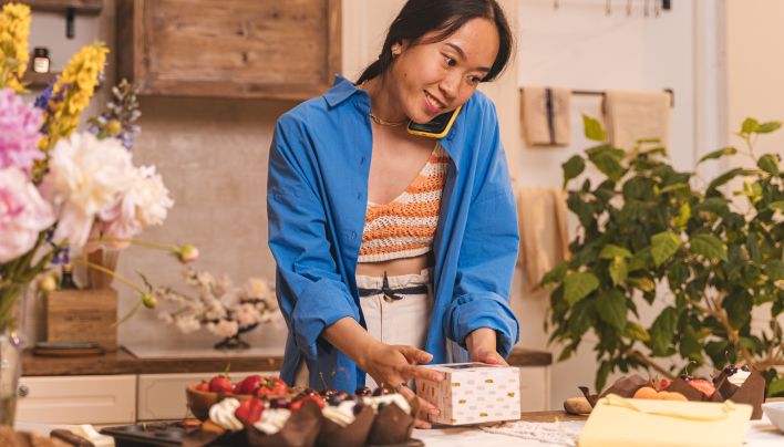 A Woman Talking on Her Phone While Boxing Pastry